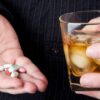 copo com bebida alcoólica ao lado de comprimidos sobre a mesa
