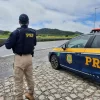 Agente da PRF segurando sua arma ao lado do carro