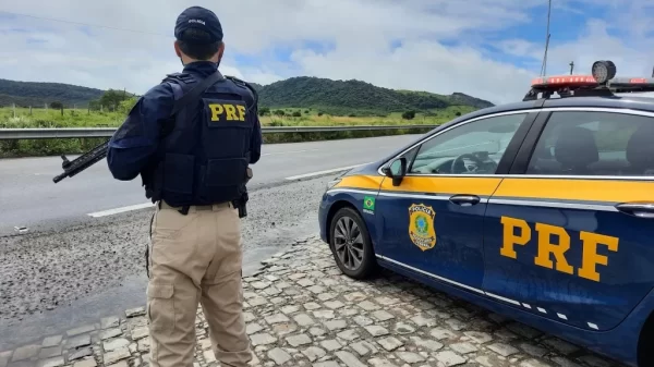 Agente da PRF segurando sua arma ao lado do carro